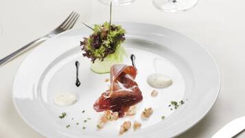 A white plate with a piece of prosciutto, a small salad, and two dollops of sauce.