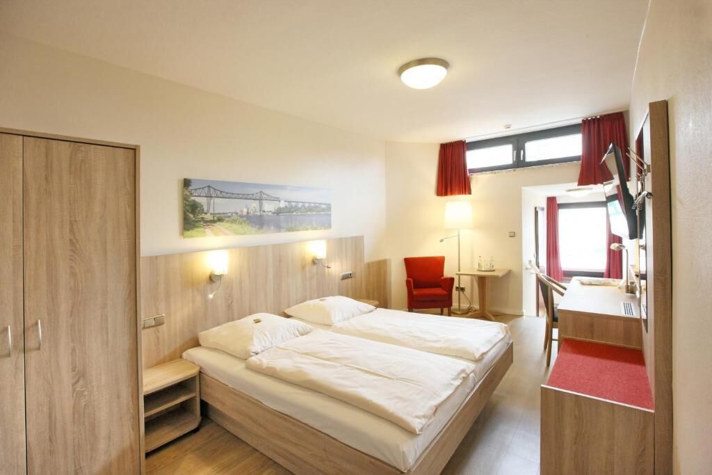 A hotel room with two beds, a desk, a chair, a wardrobe, and a painting of a bridge.