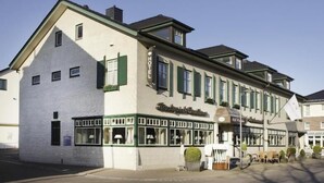 Un hôtel à la façade blanche, aux volets verts et à l’enseigne portant l’inscription « Hôtel ».