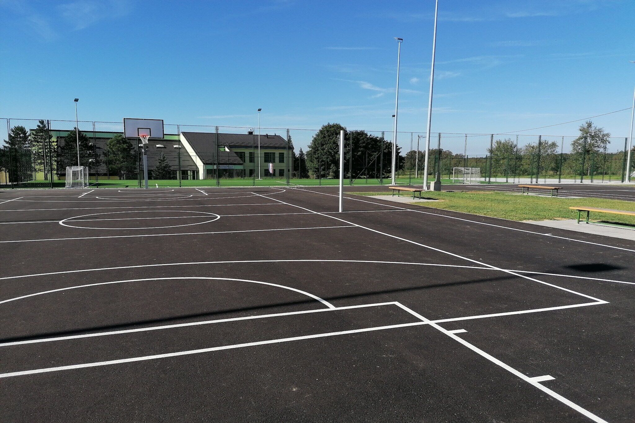 An outdoor basketball court with clear markings, a goal, and a building in the background.