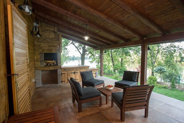 A covered patio area with wooden furniture and a stone fireplace.