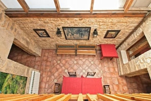 A room with a stone wall, wooden beams, a red tablecloth, and a framed picture on the wall. - La Morada del Cid (Burgos)