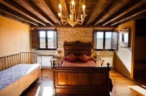 A bedroom with a wooden bed, a stone wall, and a chandelier. - La Morada del Cid (Burgos)