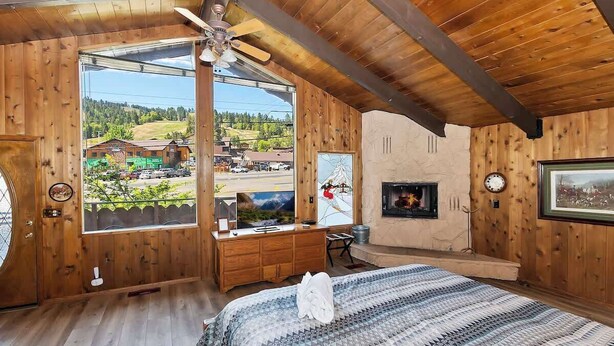 Habitación de cabaña de madera con una ventana grande, chimenea, cama y televisor.
