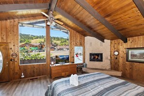 Une pièce de style cabane en bois, dotée d’une grande fenêtre, d’une cheminée, d’un lit et d’un téléviseur.