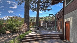 Una terraza de madera con mobiliario exterior, un espacio de estar cubierto y vistas a un área boscosa.