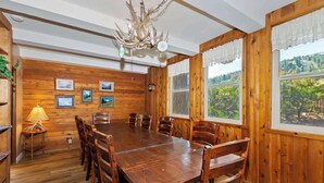 Comedor con paneles de madera, una gran mesa y sillas, cuadros en la pared y una araña.