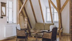 Un espacio tipo loft con vigas de madera a la vista, un sofá, dos sillones de mimbre y una pequeña mesa redonda.