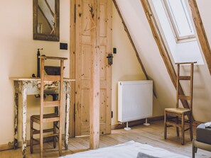 A room with a sloped ceiling, a wooden door, a radiator, a desk, a chair, and a ladder.