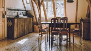 Una cocina rústica con una mesa y sillas de madera, un ventanal con vistas a árboles y una lámpara colgante.
