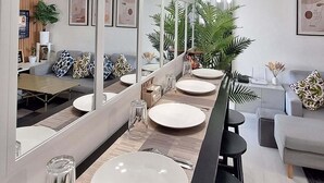 A modern dining area with a long table set for four, a large mirror reflecting the space, and hanging pendant lights. - Azure Urban Resort Staycation-First ever large scale man made beach in the City. (Parañaque)