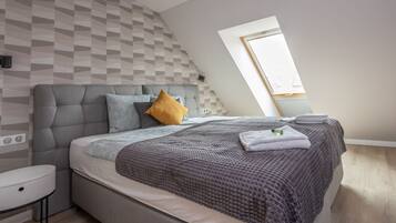 A modern bedroom with a loft-style ceiling, a grey upholstered headboard, a patterned wall, and a small bedside table.