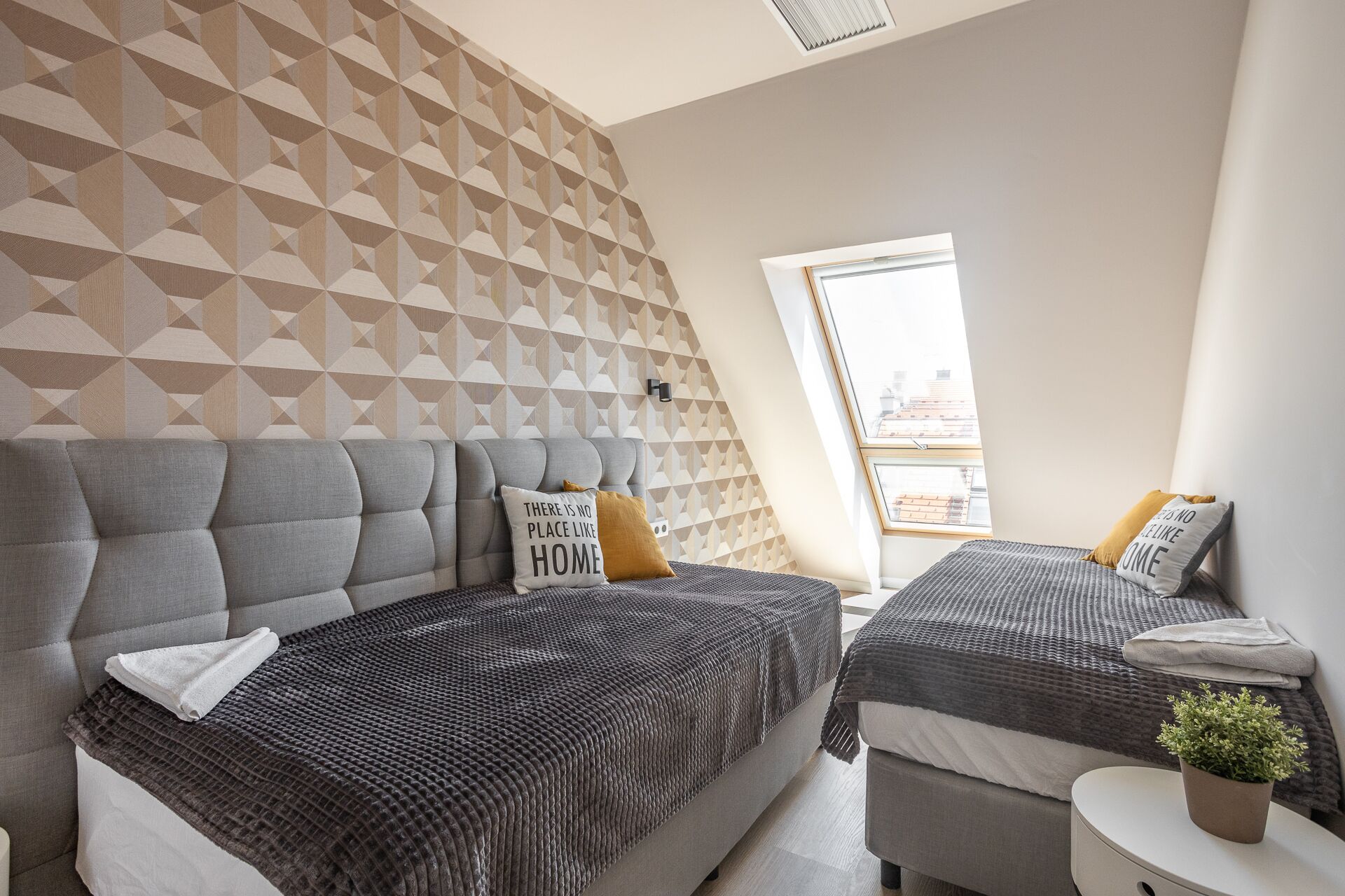 Une chambre moderne avec deux lits, un papier peint à motifs géométriques et une vue sur la ville grâce à une lucarne.