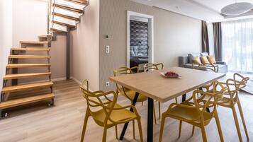 A modern living room with a wooden staircase, a dining area with yellow chairs, and a sofa with cushions.