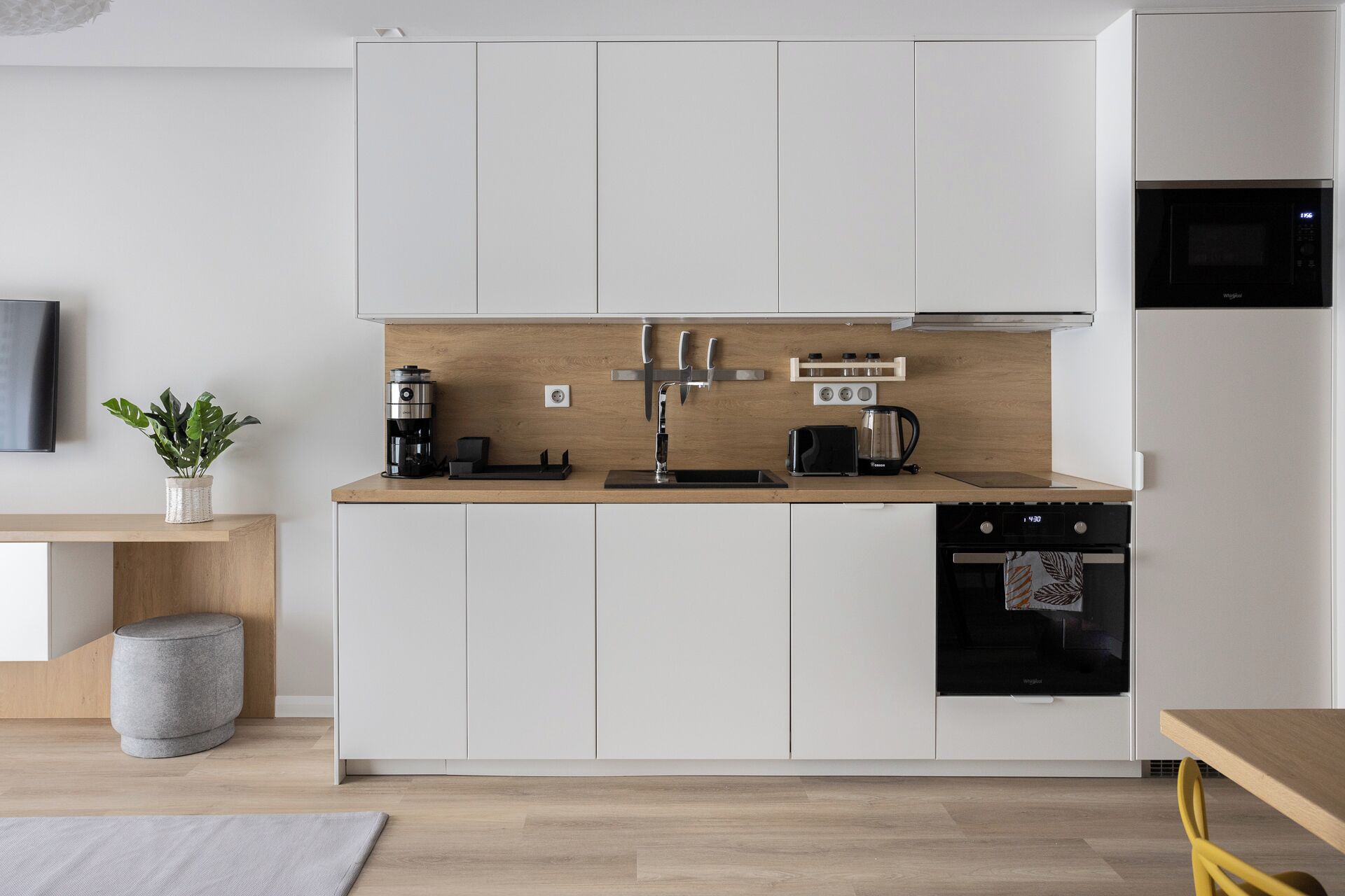 Una cocina moderna con armarios blancos, encimera de madera, cafetera, tostadora y microondas.