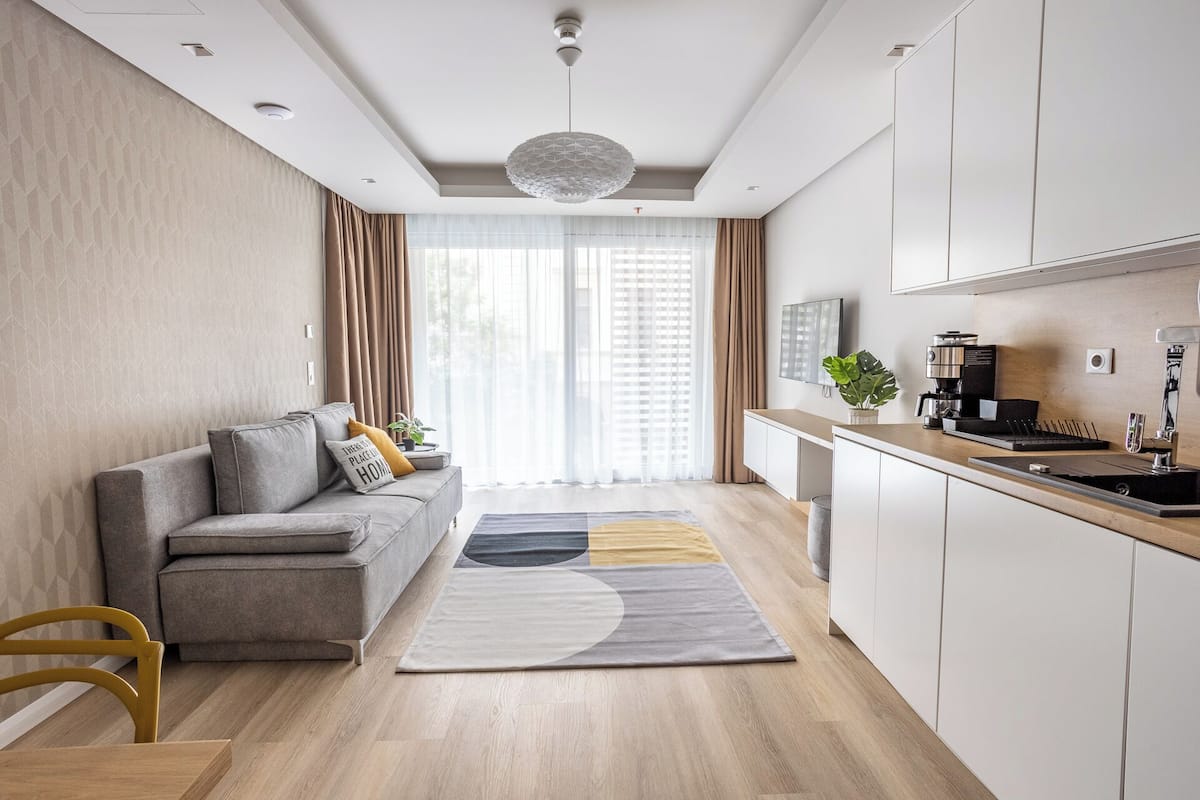 A modern living room with a grey sofa, a coffee machine, and a kitchen area with white cabinets.