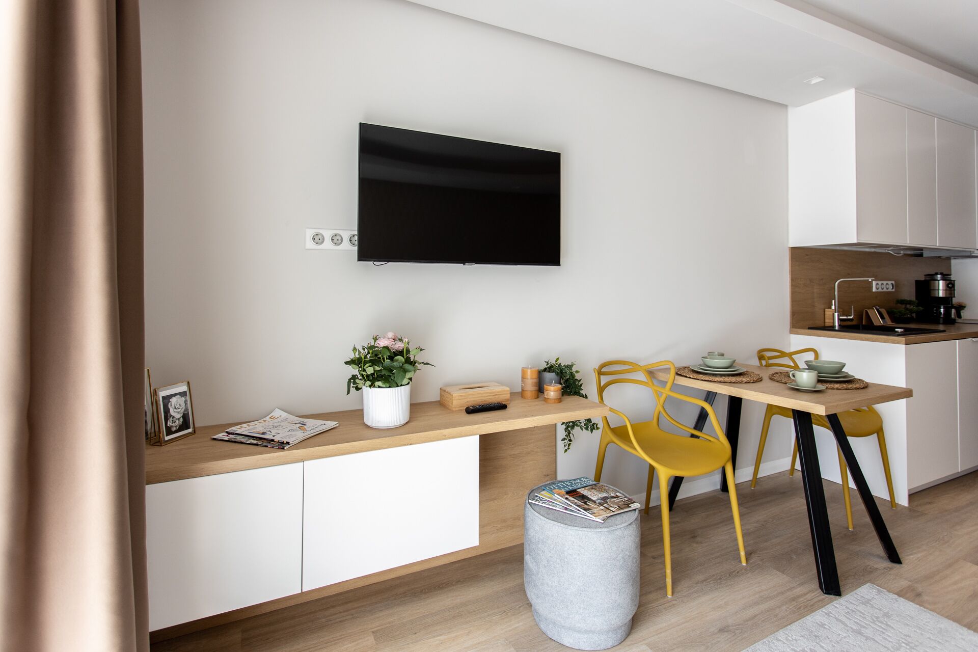 Una cocina moderna con televisor de pantalla plana, armarios de madera y un comedor con sillas amarillas.