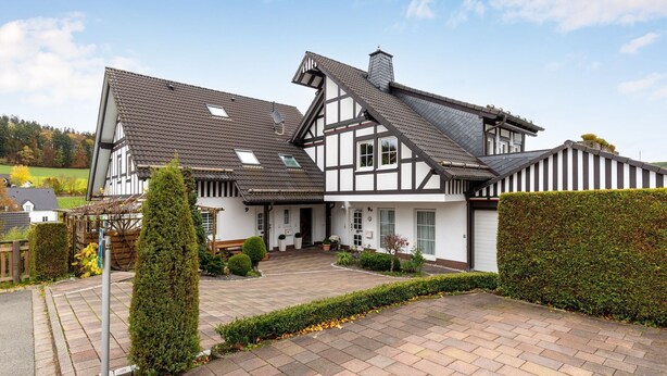 A traditional half-timbered house with a sloped roof, a front porch, and a driveway leading to the entrance. - Gemütliche Ferienwohnung am Waldrand (Eslohe)