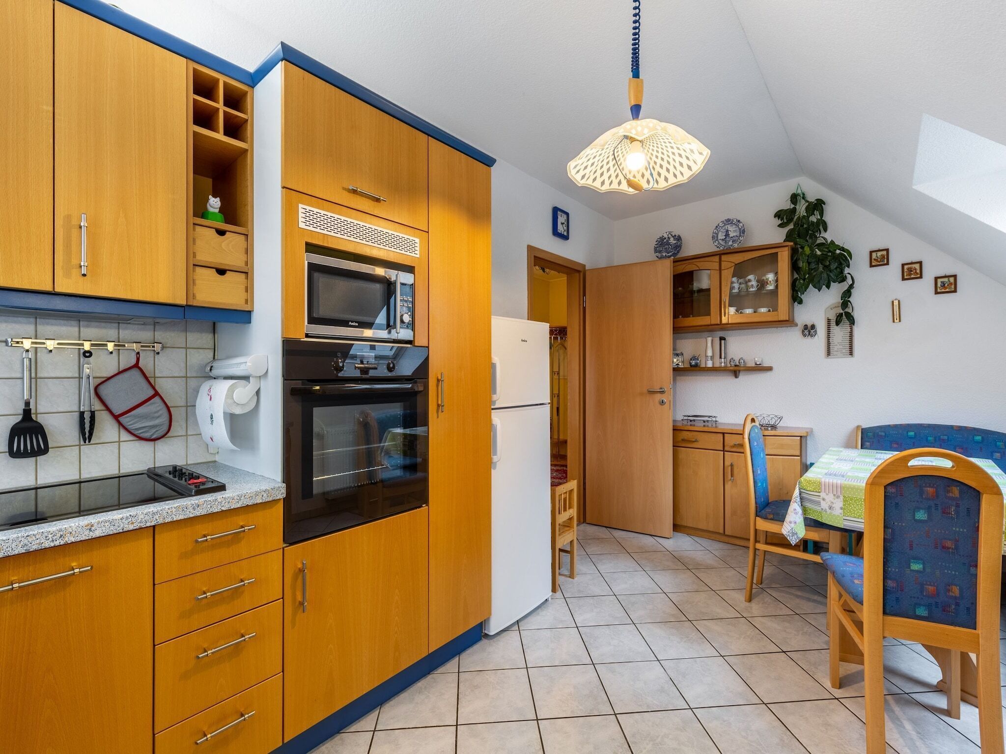 A compact kitchen with wooden cabinets, a microwave, oven, and a refrigerator. There is a dining area with a table and chairs.