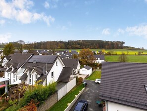 Un barrio residencial con casas de tejados inclinados y paneles solares, rodeado de campos verdes y árboles.