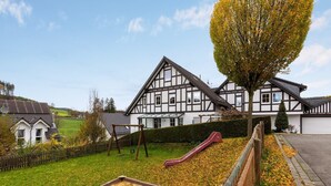 A traditional half-timbered house with a large garden, a wooden swing set, and a slide. - Gemütliche Ferienwohnung am Waldrand (Eslohe)