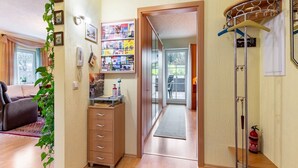A hallway with a wooden floor, a red patterned rug, a wooden cabinet, and a shelf with various items. - Gemütliche Ferienwohnung am Waldrand (Eslohe)