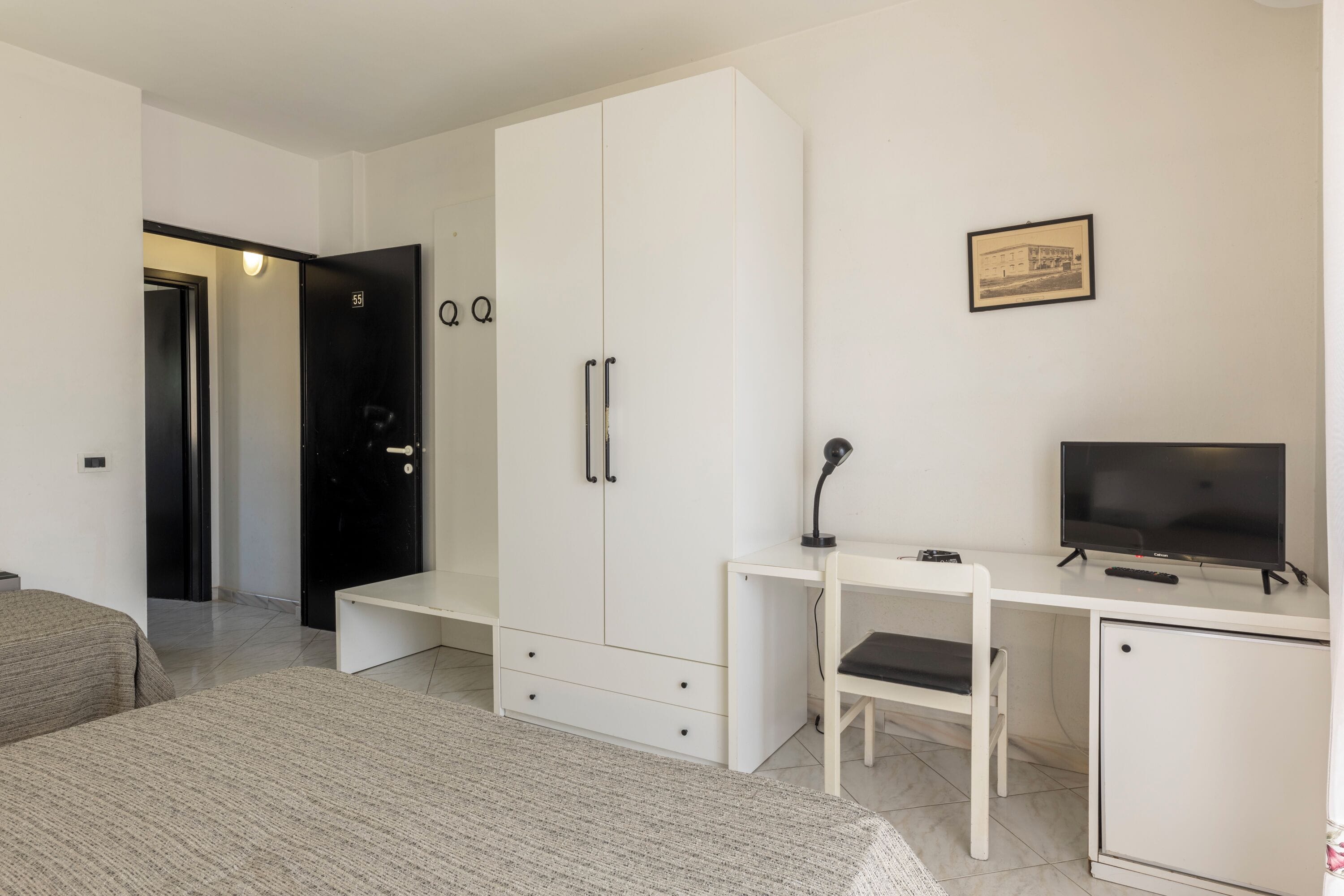 A modern bedroom with a bed, a desk with a chair, a television, and a wardrobe.