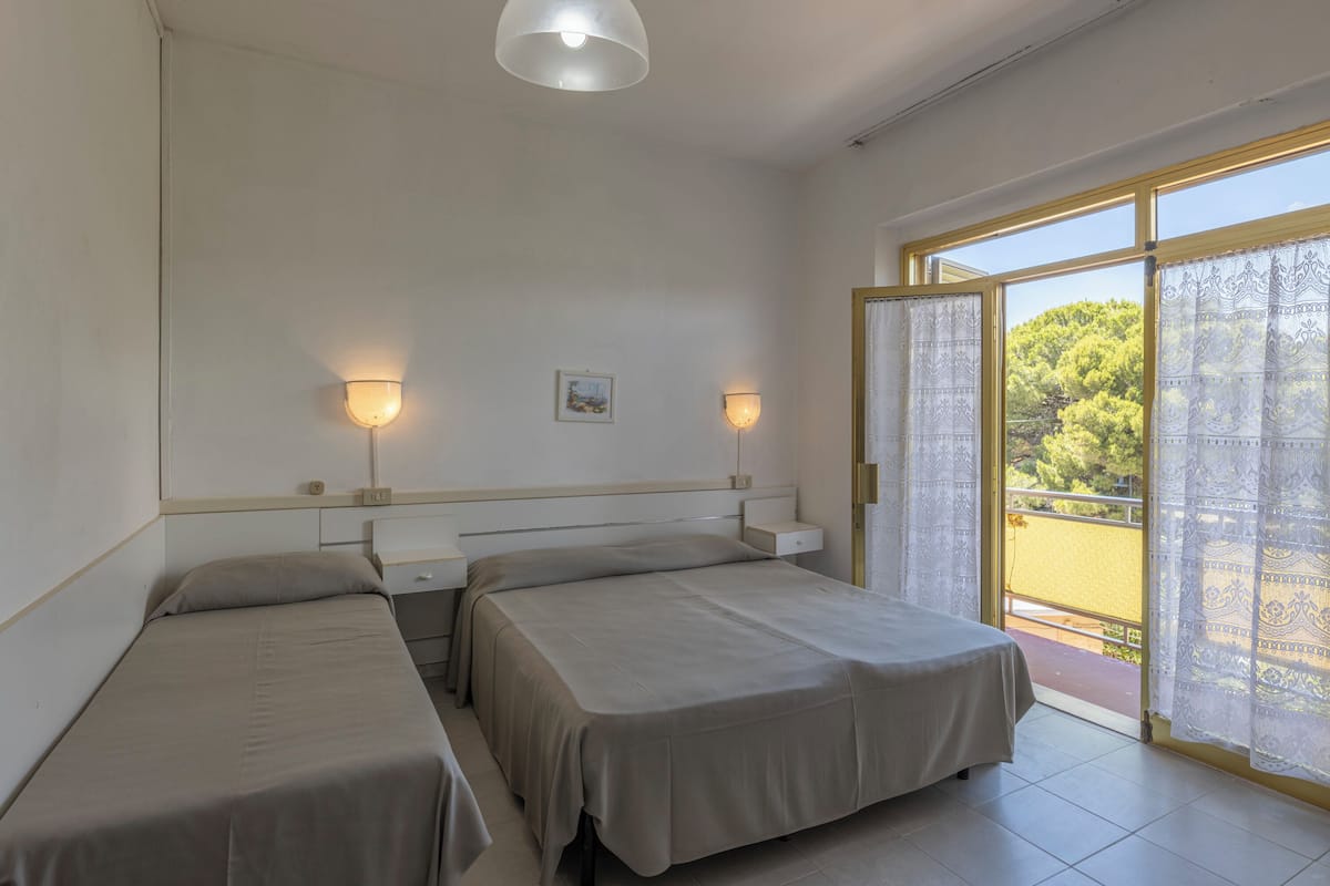 Ein Zimmer mit zwei Betten, einem kleinen Tisch und einem Fenster mit Vorhängen.