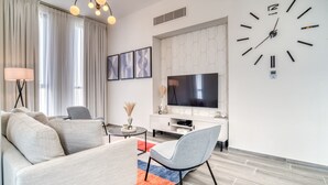 Un salon moderne avec un canapé, un fauteuil, un téléviseur et une grande horloge murale.