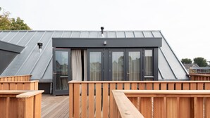 Een modern gebouw met een schuin dak, grote glazen deuren en een houten terras.