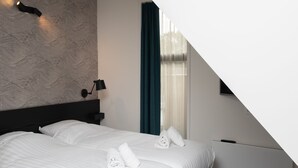 Een moderne hotelkamer met een groot bed, een hoofdeinde met een lamp en een raam met gordijnen.