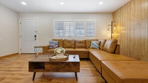 A living room with a brown leather sectional sofa, a wooden coffee table with a tray and vase, and a white door.