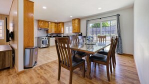 A modern kitchen with wooden cabinets, a stainless steel stove, and a dining area with a glass table and wooden chairs.