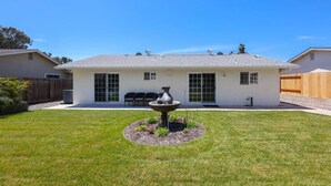 A single-story house with a fenced backyard, a patio with outdoor furniture, and a decorative fountain.
