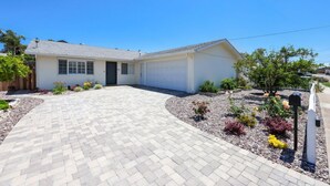 A single-story house with a garage, paved driveway, and landscaped garden with various plants and flowers.