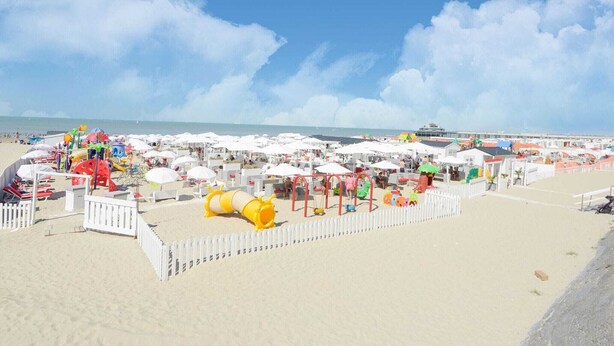 A beach with white umbrellas and a fenced area with children's play equipment. - Simplistic Apartment in Blankenberghe near Belgium Pier (Blankenberghe)