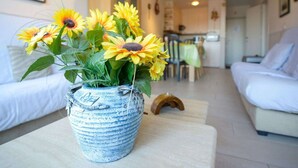 A living room with a blue vase containing sunflowers on a wooden table, a white sofa, and a dining area in the background. - Simplistic Apartment in Blankenberghe near Belgium Pier (Blankenberghe)
