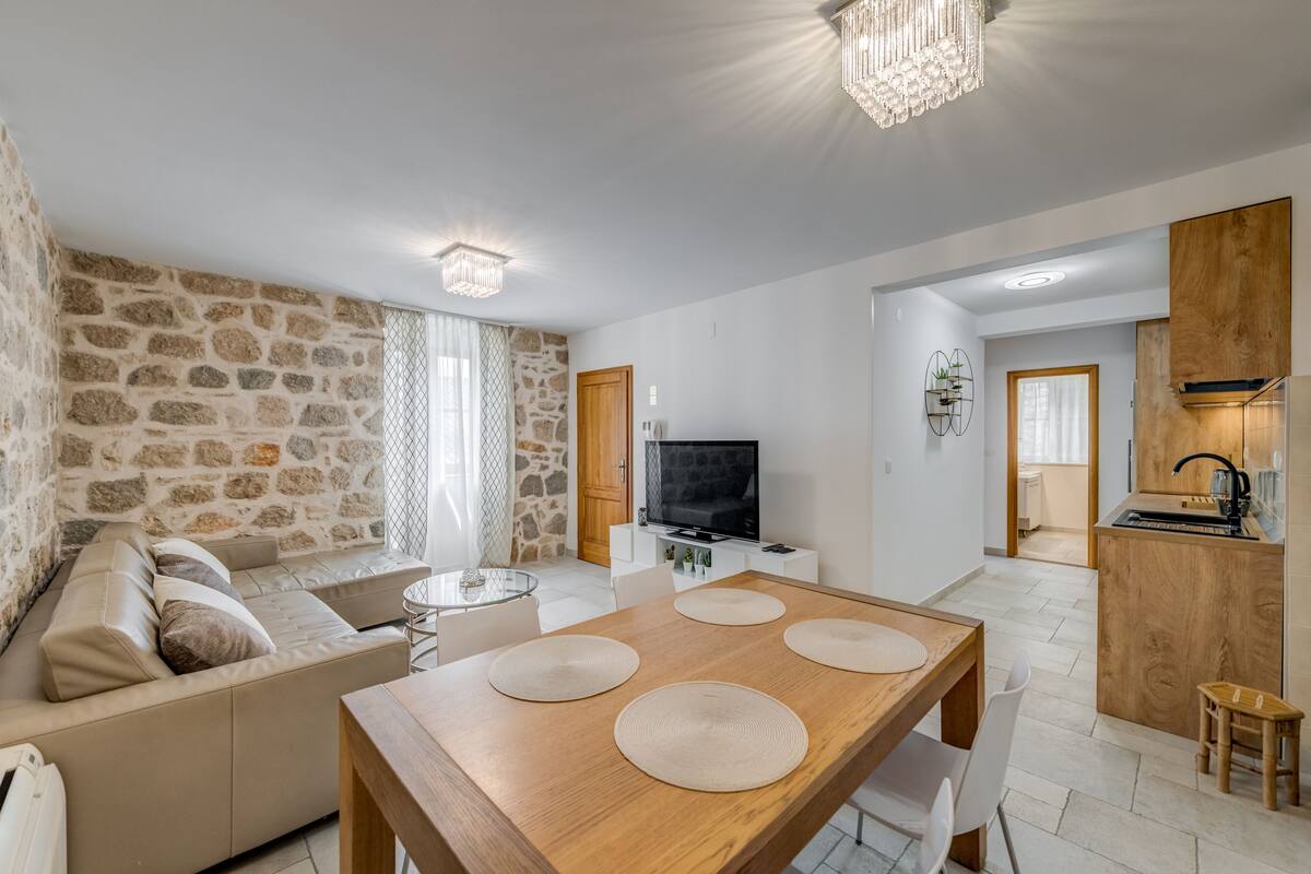 A modern living room with a stone wall, a wooden dining table, a sofa, and a TV.