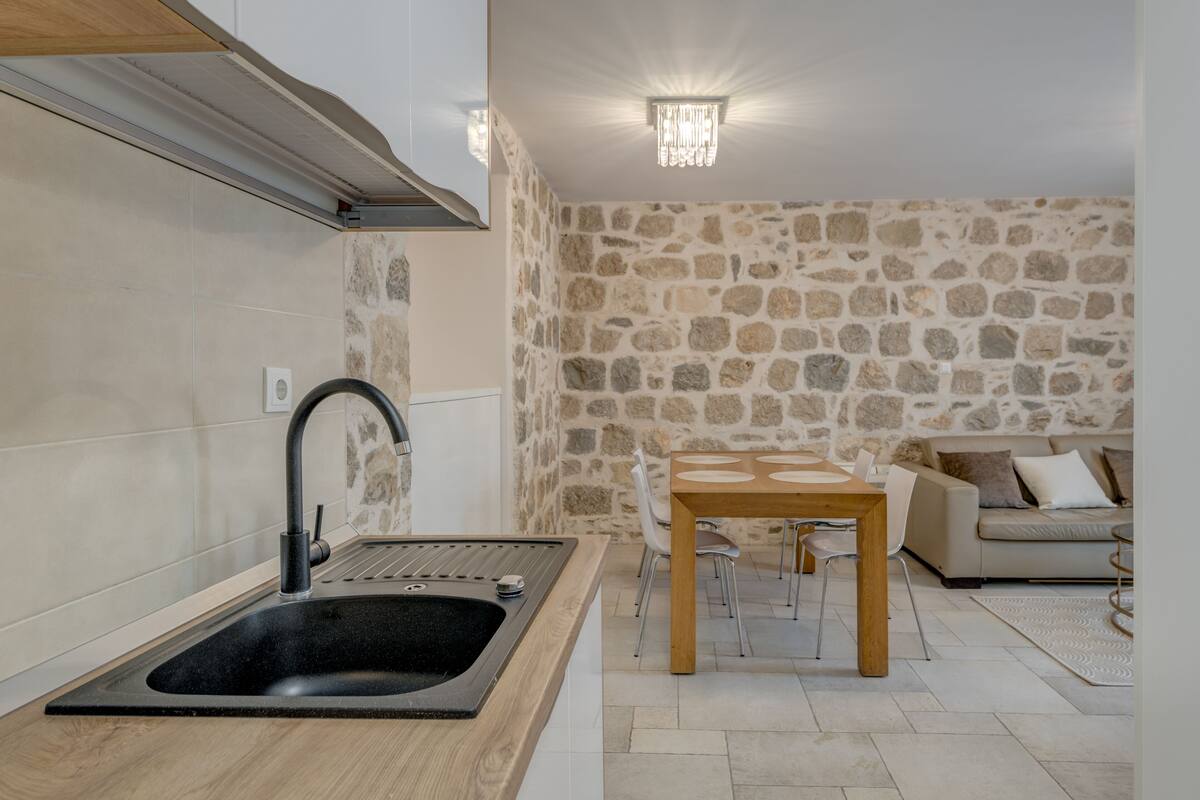 A modern kitchen with a black sink, a stone wall, and a dining area with a wooden table and chairs.