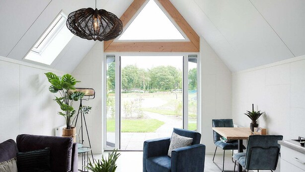 Ein modernes Loft mit schräg genehmter Decke, einem Essbereich und einem großen Fenster mit Blick auf einen Garten.