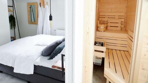 Ein Schlafzimmer mit einem Bett, einer Hängelampe und einer sichtbaren Holzauna hinter einer offenen Tür.