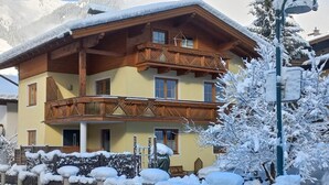 Ein mehrstöckiges Holzgebäude mit Balkonen, umgeben von schneebedeckten Zäunen und Bäumen.