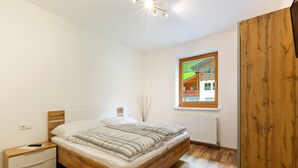 Ein Schlafzimmer mit einem hölzernen Bett, einem Nachttisch, einer Heizung und einem Fenster mit Blick auf ein Haus.