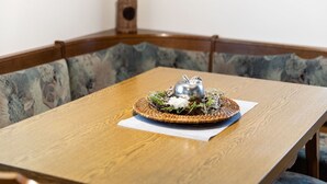 Ein Esstisch mit einer gewebten Tischmatte, einer silbernen Apfelschale und einer kleinen Topfpflanze im Hintergrund.