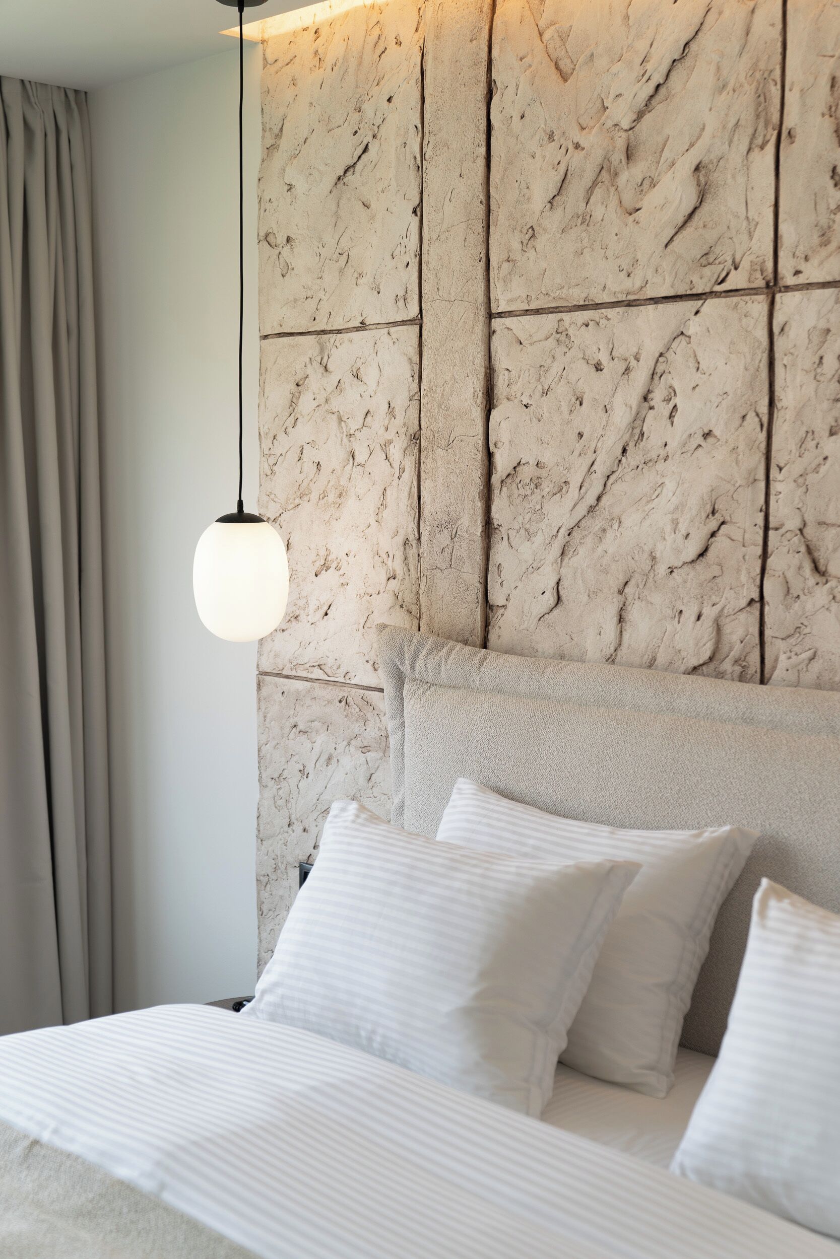 A bed with white bedding and pillows, a marble-patterned headboard, and a hanging light fixture.