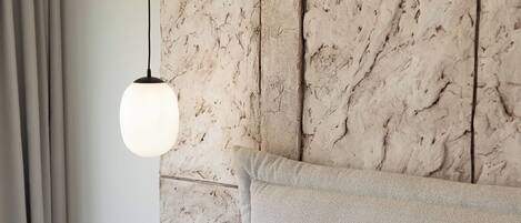 A bed with white bedding and pillows, a marble-patterned headboard, and a hanging light fixture.