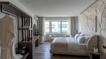 A modern bedroom with a large bed, a seating area, a wardrobe, and a view of the city.