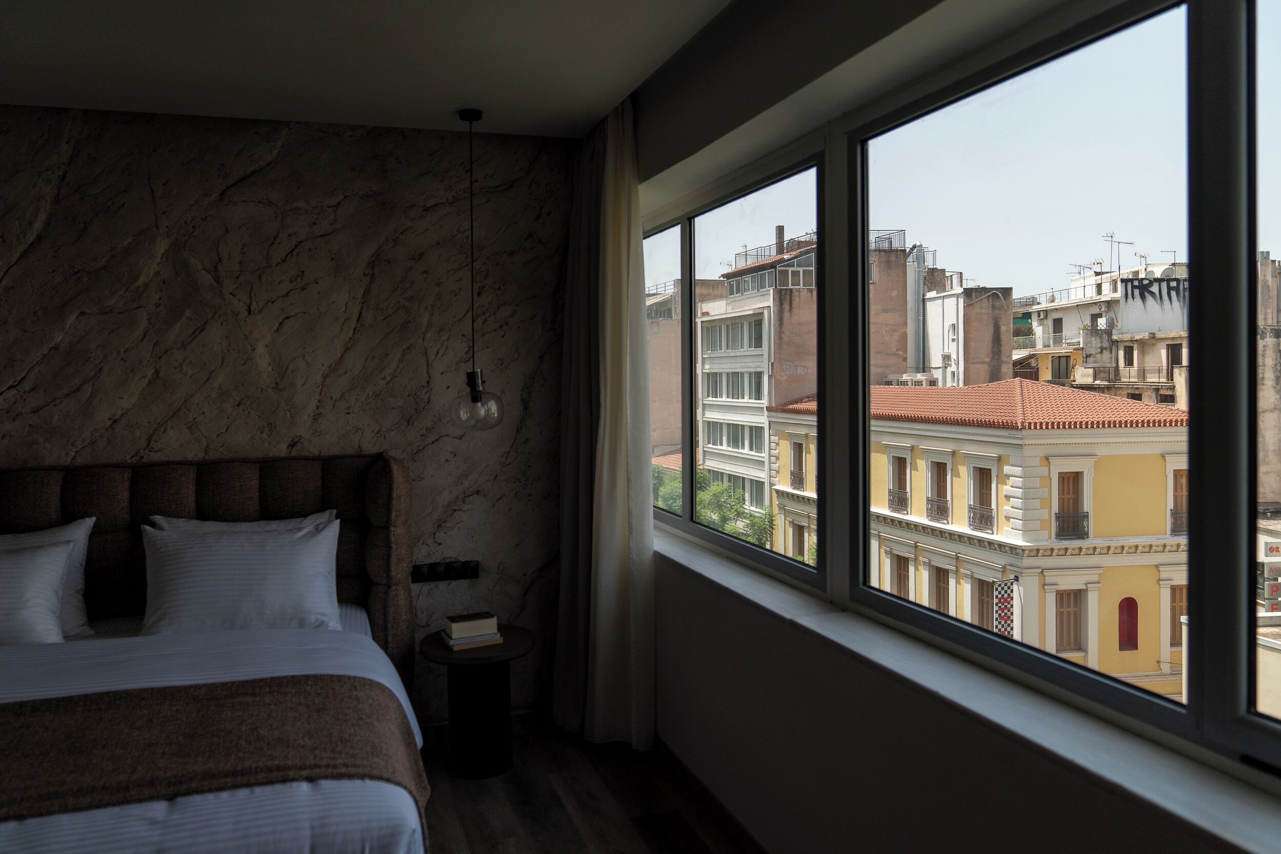 Ein Schlafzimmer mit großem Fenster, einem Bett, einem Nachttisch und einer Marmorwand.