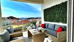 A balcony with wicker furniture, a dining table, and a view of a coastal landscape. - Villa 19 Julia apartment with sea view and 3 bedrooms (Tribunj)