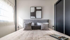 A modern bedroom with a large bed, a grey headboard, and a framed abstract painting above it. - Fantastic 1 Bedroom In City Center - isrentals (Jerusalem)